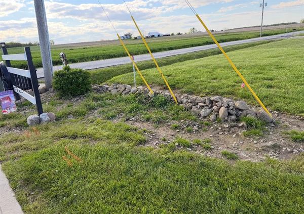 Rough patchy ground with piled rocks beside a utility pole and road.
